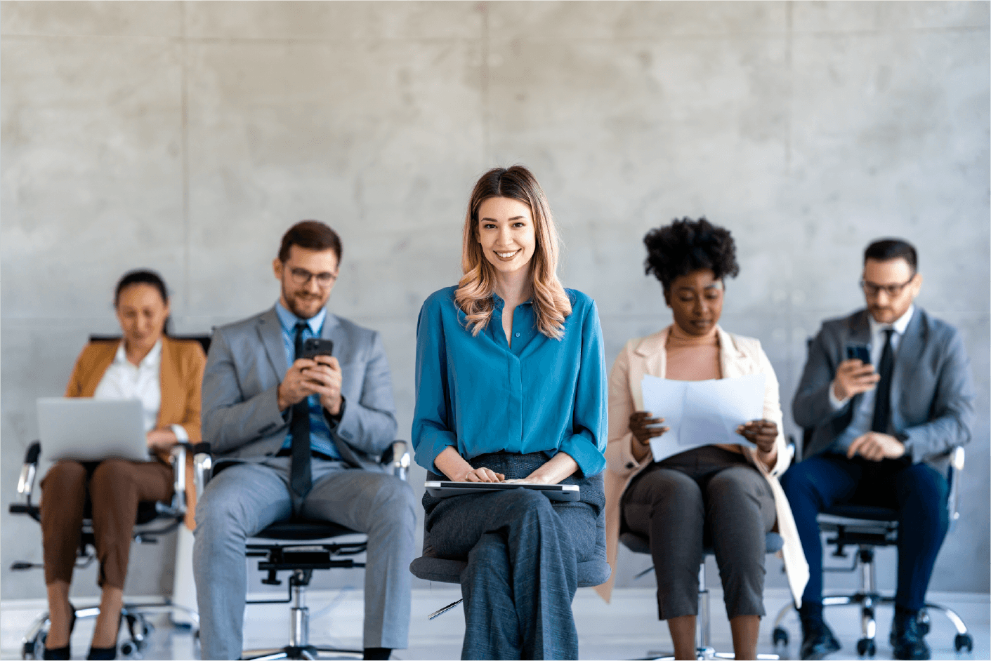 Group of diverse professionals sitting in office chairs with one woman smiling in front