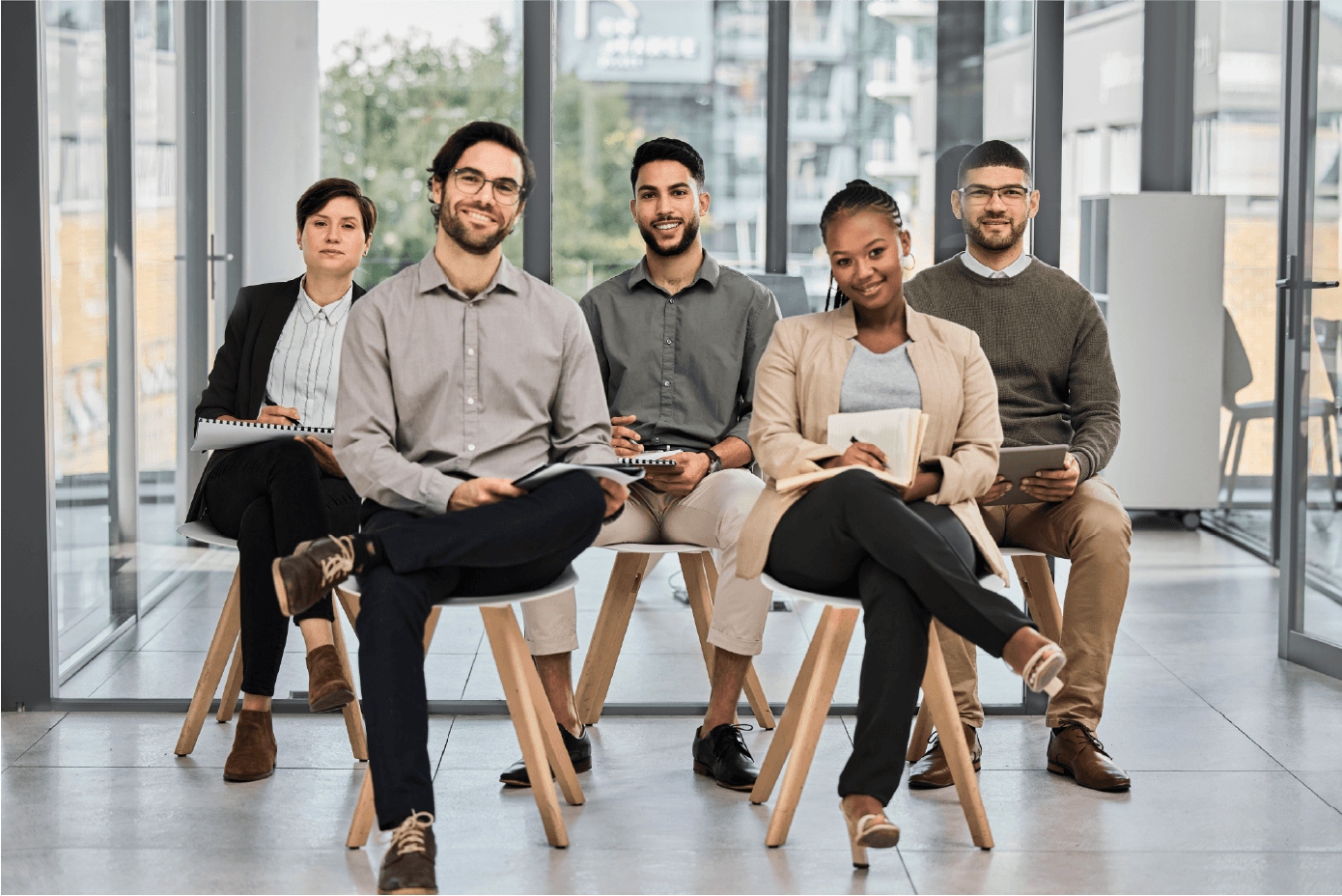 Group of diverse professionals sitting in office chairs with one woman smiling in front
